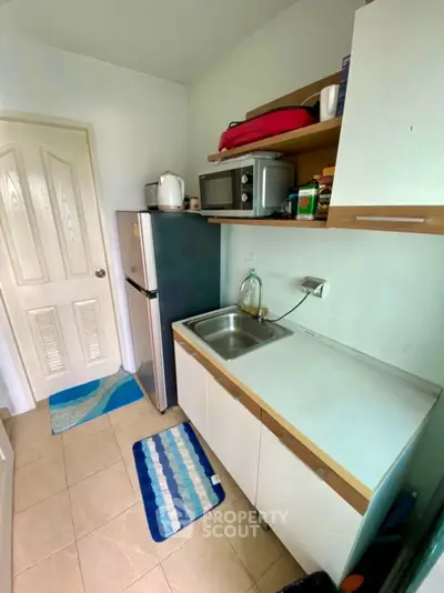 Compact kitchen with fridge, microwave, and sink in cozy apartment.