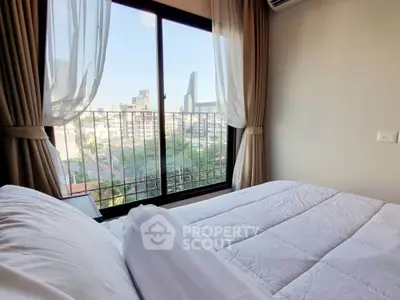 Cozy bedroom with city view from large window, featuring elegant curtains and plush bedding.