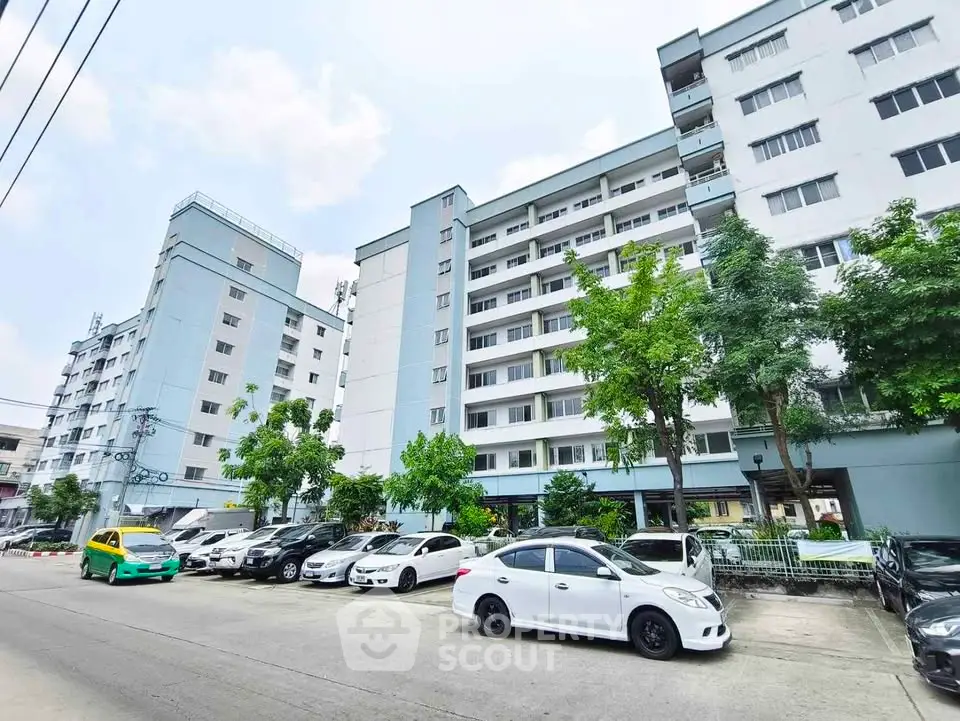 Modern apartment building with ample parking and lush greenery in urban setting.