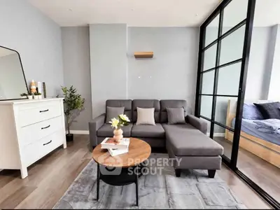 Modern living room with stylish gray sofa and glass partition leading to bedroom