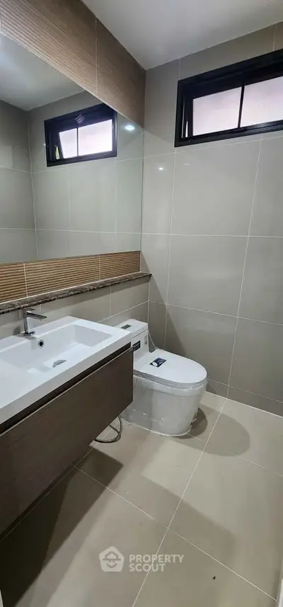 Modern bathroom with sleek fixtures and neutral tiles, featuring a stylish vanity and toilet.