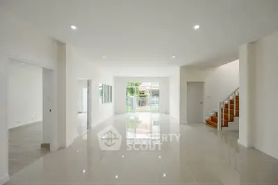 Spacious modern living room with glossy tile flooring and staircase, ideal for family gatherings.