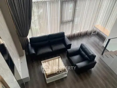 Spacious modern living room with sleek black leather furniture and large windows for natural light.