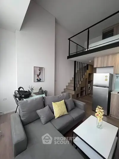 Modern loft apartment with stylish living room and kitchen area, featuring a cozy gray sofa and sleek staircase.