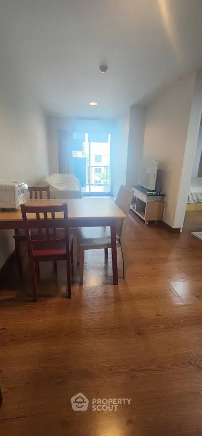 Spacious living room with wooden flooring and modern furniture, leading to a bright balcony view.