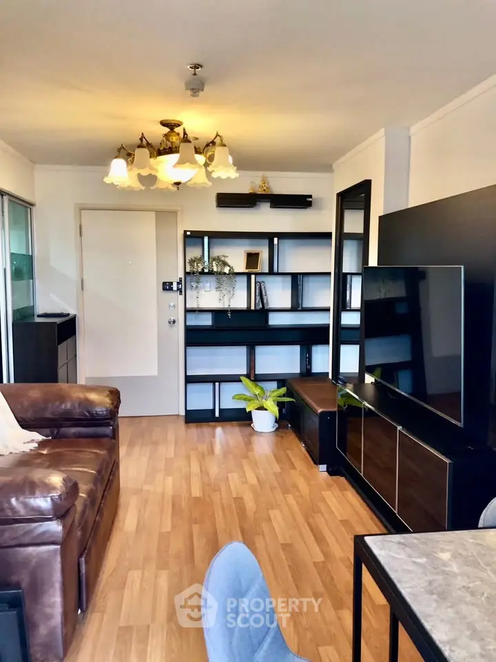 Modern living room with leather sofa, stylish shelving, and large TV in a cozy apartment setting.