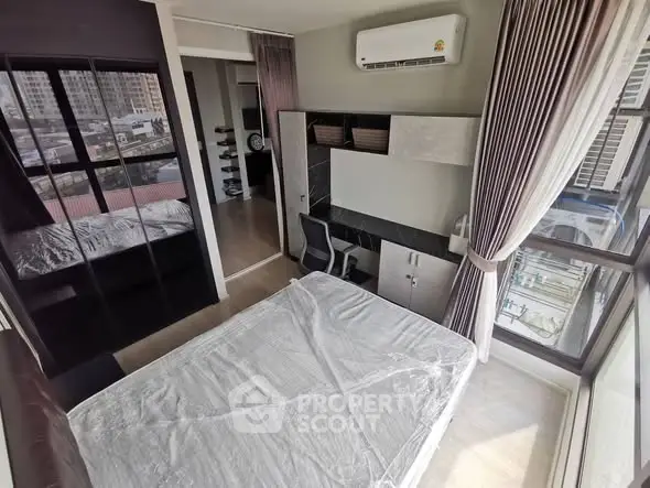 Modern bedroom with large windows and city view, featuring a desk and air conditioning.