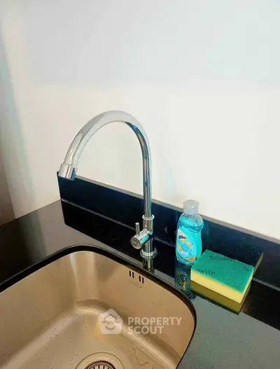 Modern kitchen sink with sleek faucet and granite countertop, featuring dish soap and sponge for convenience.