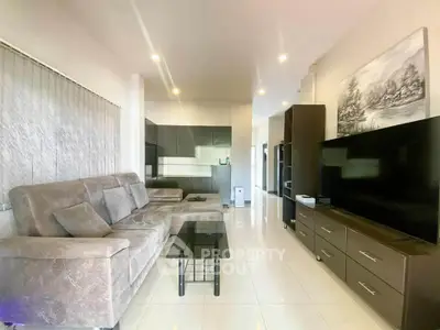Spacious modern living room with sleek furniture and large TV, perfect for relaxation.
