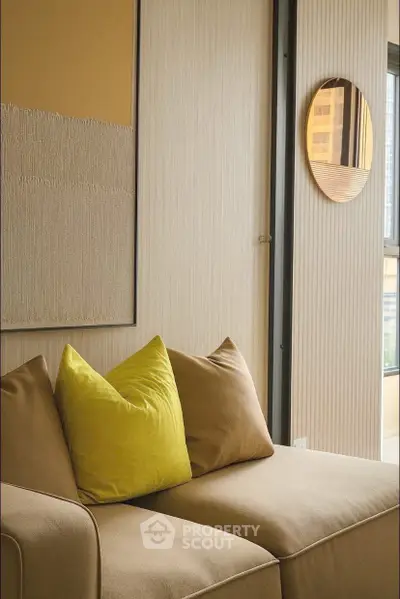 Modern living room with beige sofa and vibrant yellow pillow, featuring stylish wall decor and natural light.