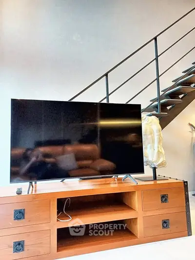 Modern living room with sleek staircase and large flat-screen TV on wooden console.