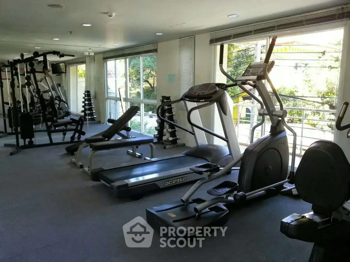 Spacious gym with modern equipment and large windows offering natural light and outdoor views.
