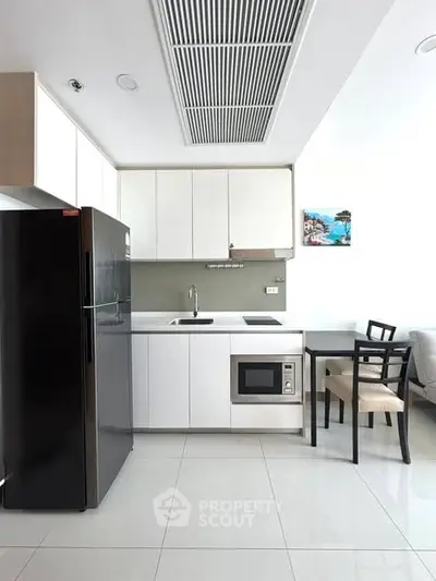 Modern kitchen with sleek white cabinets, black fridge, and dining area in a contemporary apartment.
