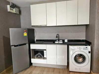Modern kitchen with sleek appliances including fridge, microwave, and washing machine in compact layout.