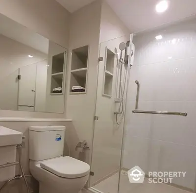 Pristine white-tiled bathroom with glass shower enclosure, modern fixtures, and built-in shelving, reflecting a clean and minimalist design.