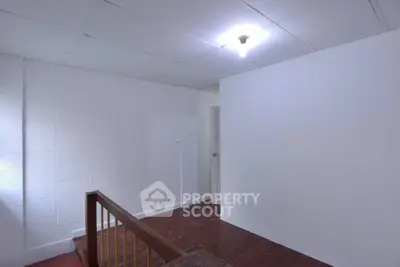 Minimalist interior with white walls and wooden flooring, featuring a staircase and simple lighting.