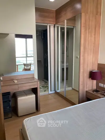 Modern bedroom with wooden accents and mirrored closet doors, featuring a cozy vanity area and natural light.