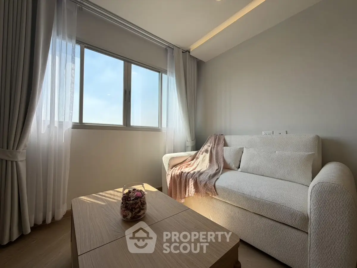 Cozy living room with natural light, featuring a plush sofa and elegant curtains, perfect for relaxation.