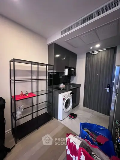 Modern apartment entryway with sleek kitchen and washing machine, showcasing contemporary urban living.