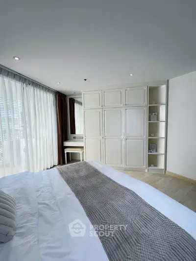 Spacious bedroom with elegant built-in wardrobe and natural light from large windows.