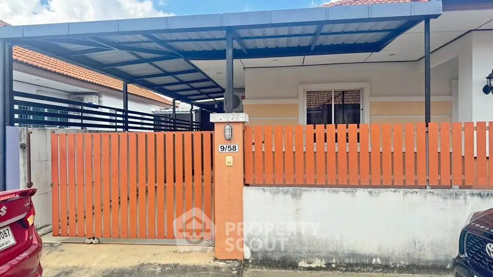 Charming single-story home with covered carport and vibrant orange fence in a serene neighborhood.