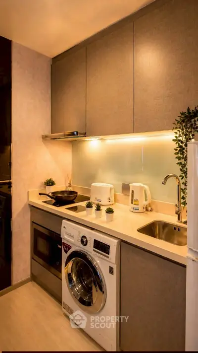 Modern kitchen with washing machine, oven, and sleek cabinetry in stylish apartment.