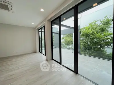 Spacious modern living room with large glass doors opening to a balcony with lush greenery.