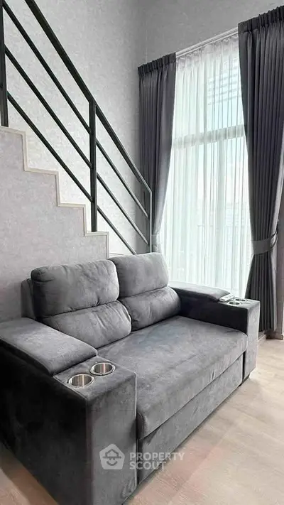 Modern living room with stylish gray sofa and large window, featuring sleek staircase design.