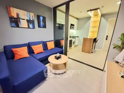 Modern living room with blue sofa and open kitchen featuring a washing machine and breakfast bar.