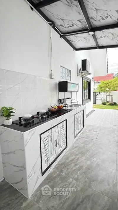 Modern outdoor kitchen with marble countertops and gas stove, featuring sleek design and garden view.