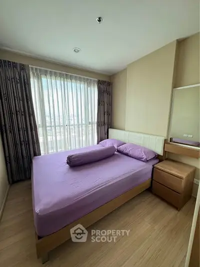 Cozy bedroom with purple bedding and large window offering natural light