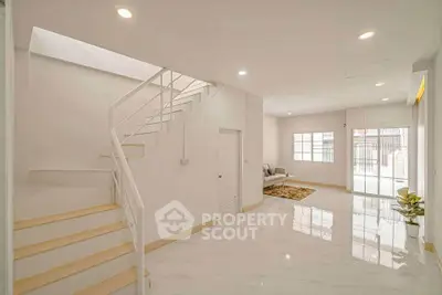 Spacious modern living room with elegant staircase and large windows for natural light.