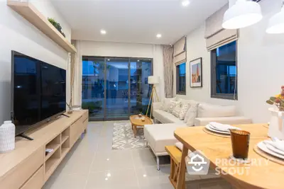 Modern living room with stylish decor and large TV, open to a spacious balcony.