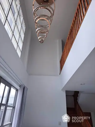 Elegant high-ceiling living space with modern chandelier and wooden staircase