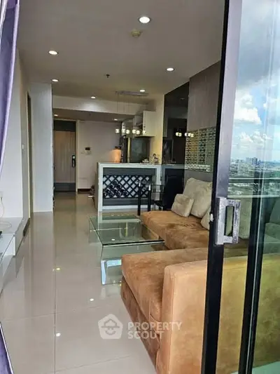 Modern living room with glass doors and city view, featuring a cozy brown sofa and sleek glass table.