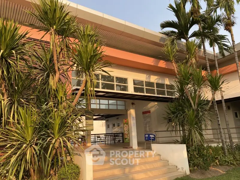 Modern building entrance with tropical landscaping and sleek architectural design.