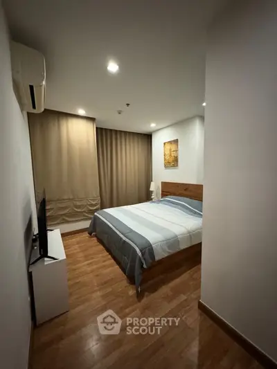 Cozy bedroom with polished wooden flooring, a comfortable queen-sized bed, and modern amenities, perfect for restful nights in a serene urban home.
