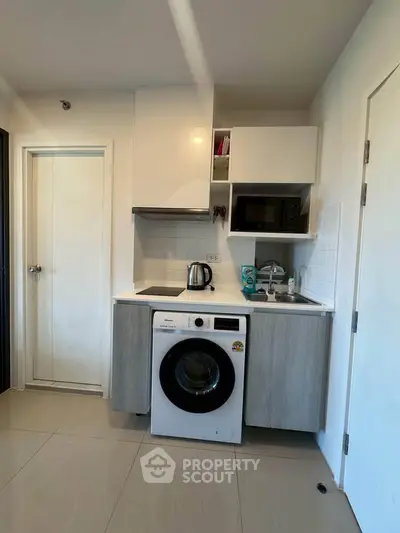 Modern compact kitchen with washing machine and microwave in a sleek apartment.