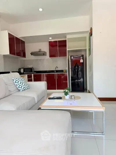 Modern living room with open kitchen, featuring sleek red cabinets and cozy white sofa.