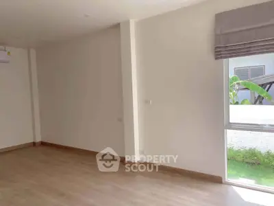 Spacious empty room with large window and wooden flooring, perfect for customization.