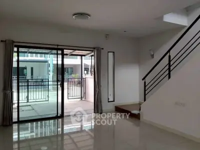 Spacious modern living room with sliding glass doors and sleek staircase, ideal for contemporary living.