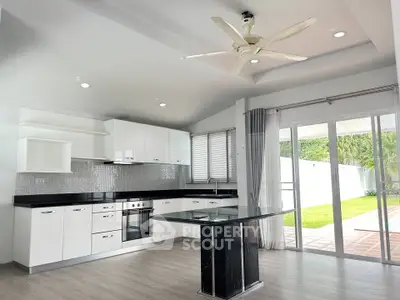 Modern kitchen with open layout and garden view, featuring sleek white cabinets and a central island.