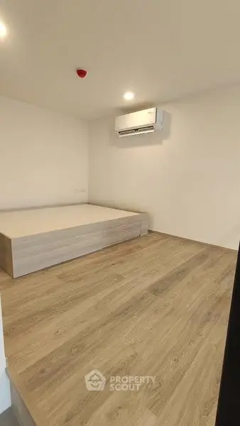 Minimalist bedroom with wooden flooring and wall-mounted air conditioner.