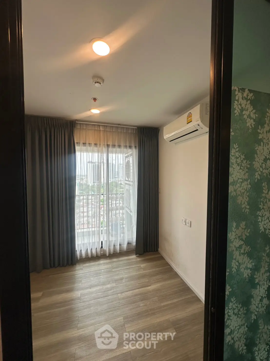 Spacious bedroom with wooden flooring and large window offering natural light and city view.