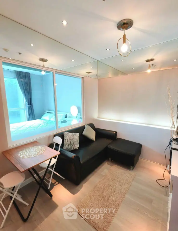 Modern living room with sleek black sofa and dining area, featuring large window and stylish lighting.