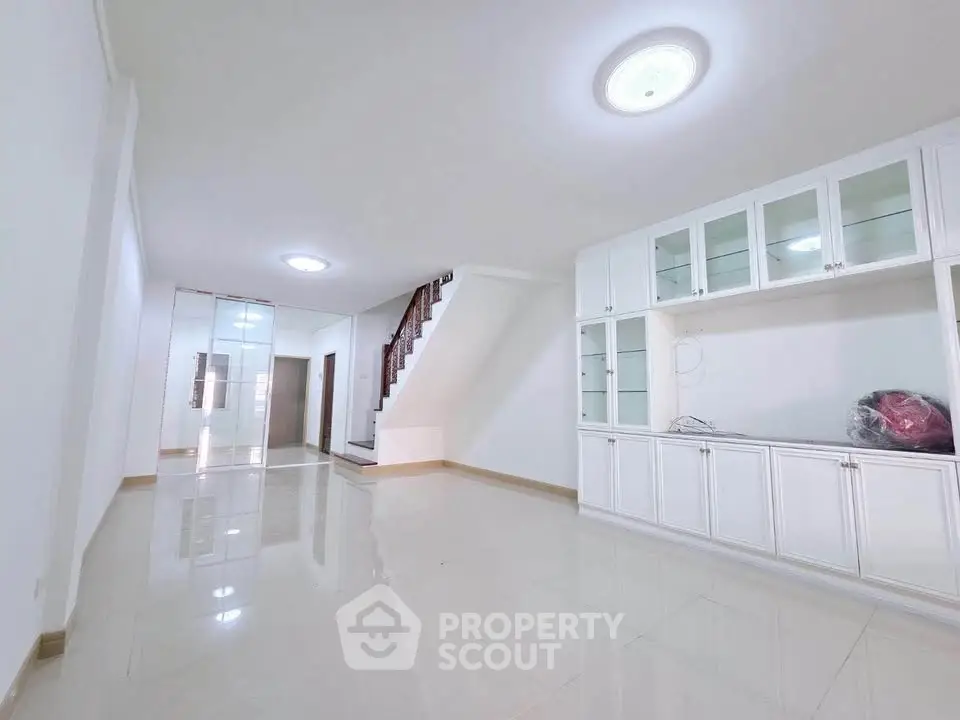 Spacious modern living room with sleek white cabinetry and elegant staircase, perfect for family gatherings.