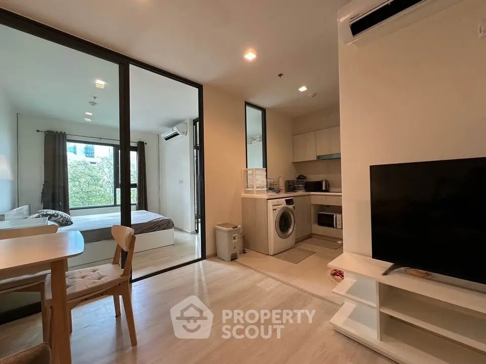 Modern open-plan apartment with kitchen, living area, and bedroom, featuring natural light and contemporary furnishings.