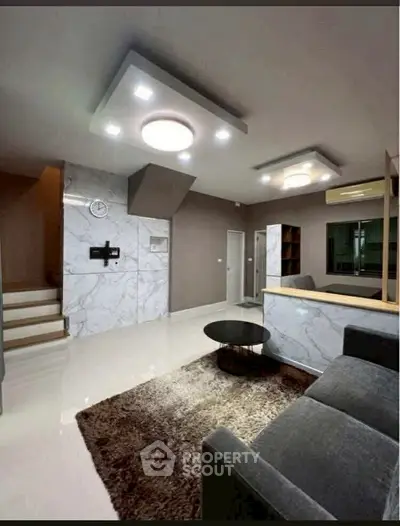 Modern living room with stylish lighting and marble accents, featuring a cozy seating area and elegant decor.