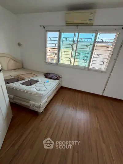 Spacious bedroom with wooden flooring and large windows offering natural light.