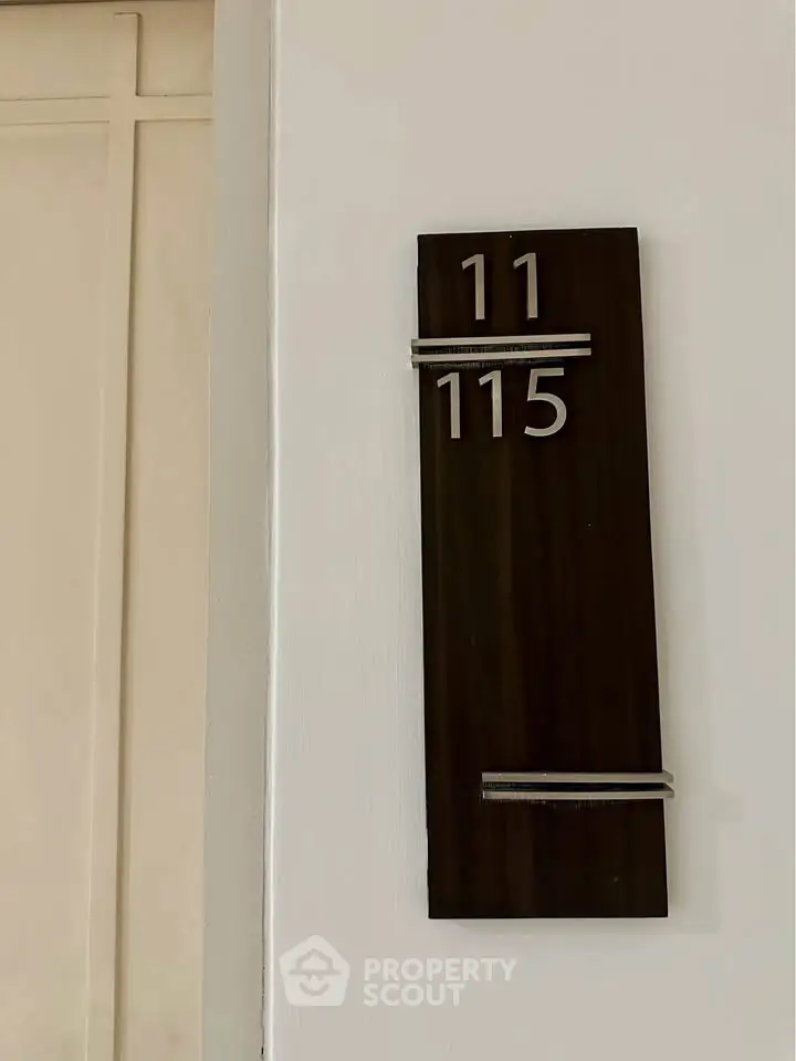 Modern apartment door number sign with sleek design on white wall.